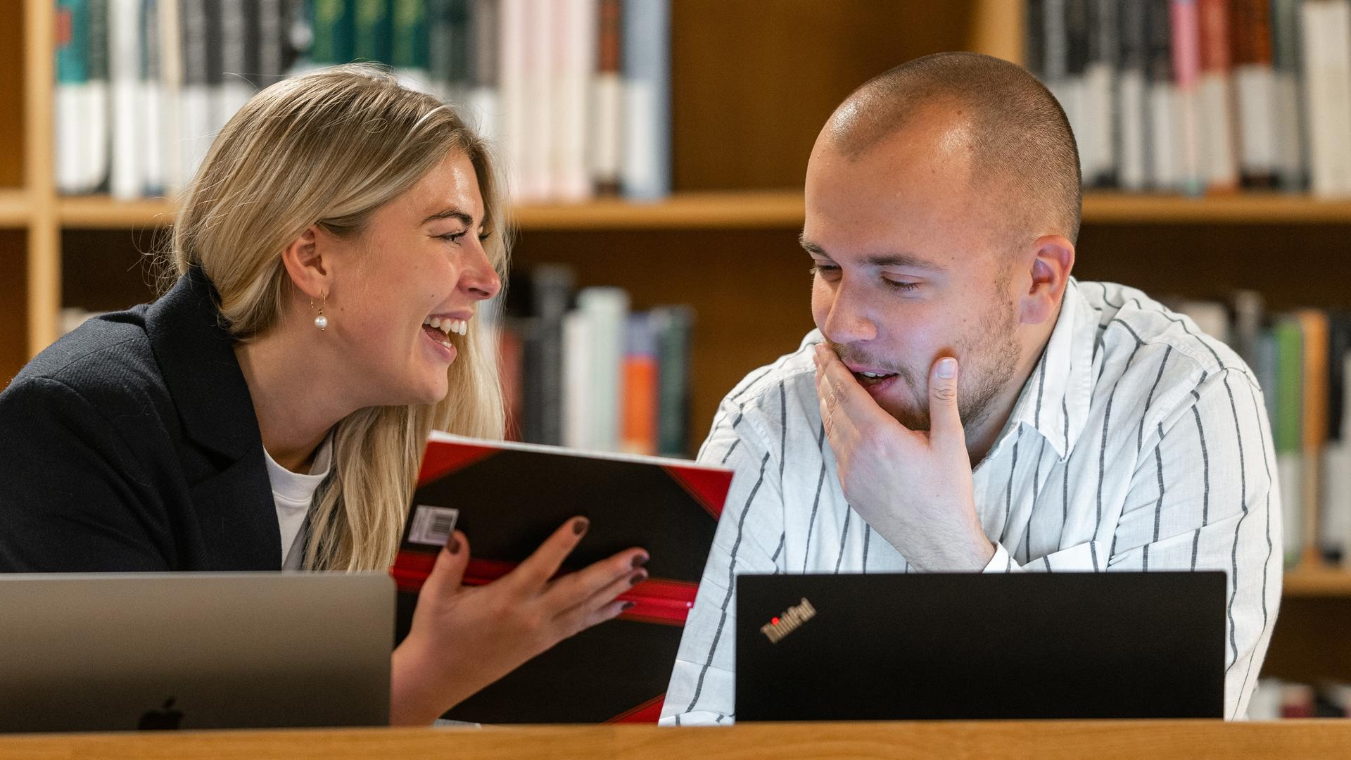 To personer arbejder sammen om en computer og en notesbog. 